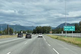 Muldoon Road arcs northwest from SR 1 by Tikahtnu Commons big box retail center to a gate into Joint Base Elmendorf-Richardson.