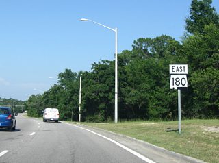 Eastbound shield for SR 180 posted on the final stretch of Fort Morgan Road between SR 59 and SR 135. A traffic signal follows at an entrance to Wal-mart.