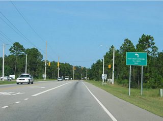 The upcoming traffic light represents the south end of the Express. The toll plaza for the bridge over Portage Creek lies north of waterway. From that point onward, the Foley Beach Express expands to four lanes with a wide grassy median. There are no interchanges along the highway and some businesses and residences have appeared adjacent to the route since its opening in 2000.