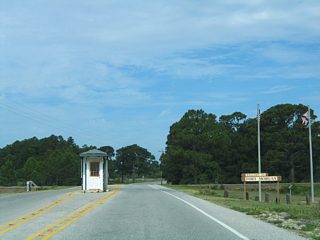SR 180 officially ends at the entrance to Fort Morgan State Park. Dixie Graves Parkway continues to the Mobile Bay Ferry and Fort Morgan within the park. Since this photo was taken, the guard house was removed and the widened stretch of roadway was reconfigured into a two lane highway. A pay station for the park now follows the ferry launch entrance.