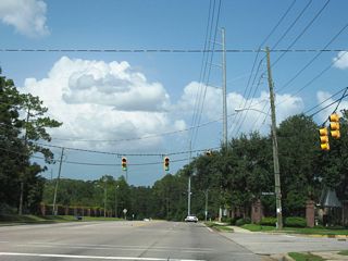 Grelot Road eastbound at Regency Oaks Drive south and Westbury Drive north. Grelot Road constitutes a four to five lane arterial joining neighborhood and retail areas east from Schillinger Road to University Boulevard.