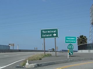 The Terminal Island Freeway curves southwest through industrial areas of Long beach to combine with SR 47 ahead of the Commodore Schuyler F. Heim Bridge onto Terminal Island. SR 47/103 overlap south to Ocean Boulevard and I-710 west of the Long Beach International Gateway bridge.