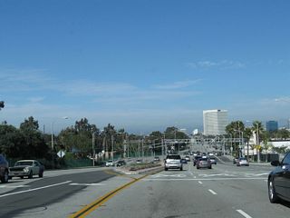 The dynamics of California 1 change as a result of entering the oil refinery area. The state route widens out to allow four northbound lanes, and the closed-in development common to the beach cities south of here becomes less common in El Segundo. The railroad tracks visible ahead serve the Chevron El Segundo Oil Refinery located on the west side of California 1. The refinery was named El Segundo since it was the second of Chevron&#039;s refineries.