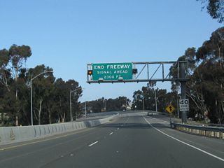 As traffic from Doheny Park Road north merges onto California 1, an overhead sign advises of the pending end of the freeway segment. The first two traffic signals along northbound are with Doheny Park Plaza and Del Obispo Street.