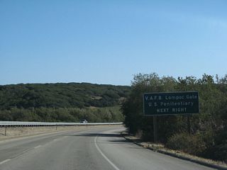 An auxiliary sign advises that Santa Lucia Canyon Road travels south to the U.S. Penitentiary and Lompoc gate to Vandenberg Space Force Base.