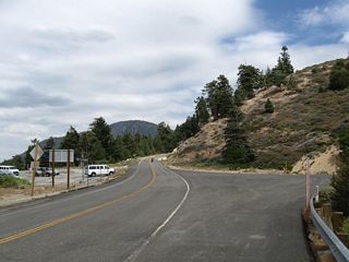 Continuing east, California 2 approaches Islip Saddle. On the left (north) side of the highway is a parking area. On the south side of california 2 is a wide shoulder and a gate that blocks off access from California 2 east to California 39 south. Closed since 1978, California 39 has not been open to motorized traffic due to a series of rock slides and other road damage. Plans call for eventual reopening of the route, but that is not expected until 2015 to 2018 at the ealiest.