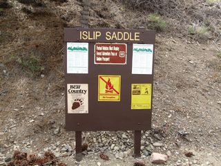 An information and regulatory sign for Islip Saddle is posted in the parking lot on the north side of California 2.