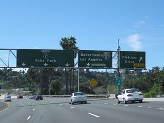 Southbound (westbound) California 2 (Glendale Freeway) meets Exit 13B, Fletcher Drive. The next exit is Exit 13A, Interstate 5 (Golden State Freeway). These porcelain enamel overhead guide signs date back to the opening of this section of California 2 freeway, which was in 1961-1962 (between San Fernando Road and Glendale Boulevard). A green overlay covers the cardinal direction of California 2 (which probably was signed as "west" but more appropriately should be signed "south" to be consistent with the general direction of the Glendale Freeway), and another overlay likely covers a U.S. 99 sign (and possibly U.S. 6 as well, although U.S. 6 was slated in the early 1960s to be shifted over to the Hollywood Freeway before it was decommissioned in 1964).