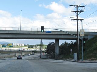 Passing under the main lanes of Interstate 5, U.S. 6 and U.S. 99/San Fernando Road enters the city of Los Angeles. This section of San Fernando Road was briefly known as U.S. 6-99 Business after the Golden State Freeway was built (as U.S. 6 and U.S. 99 were moved to the then-new freeway). After U.S. 6 and 99 were eliminated, the old route was designated as Business Loop I-5 until the 1980s. Now it is known as the historic route of U.S. 6 and U.S. 99. Here, southbound San Fernando Road meets a connecting ramp to Balboa Boulevard, which passes over San Fernando Road ahead. A Historic U.S. 99 (but not Historic U.S. 6) sign is posted on the mast arm for the ramp to Balboa Boulevard. Interstate 5 is visible to the left in this picture.