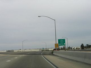 The left lane continues east onto Nina Lee Road, while the two right lanes transition onto a loop ramp that connects with the northbound truck lanes from the commercial port of entry.