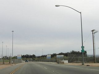 Southbound California 7 and state maintenance end at this point, just prior to the last U-Turn. A zero postmile is located in the median next to the left lane. The port of entry lies ahead.