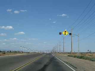 Almost as if crossing a line, development emerges along California 18 (Palmdale Road) as we skirt the southern edge of the city of Adelanto (population 31,765 as of the 2010 Census and incorporated on December 22, 1970). Several intersecting roads link California 18 with the various residential developments, many of which are master planned and are subdivisions of ranches. A traffic signal governs the flow of traffic with Monte Vista Road, and some areas appear ripe for eventual development (such as the area around Bellflower Street). Nearing U.S. 395, we find a small shopping center that offers food, gas, and other goods and services.