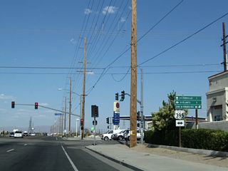 In southern Adelanto near the commercial shopping area, eastbound California 18 (Palmdale Road) meets U.S. 395 (Three Flags Highway) at this traffic signal. U.S. 395 is a major north-south corridor that originates just south of here at Interstate 15 and extends north through the Mojave Desert into the Owens River Valley and the Eastern Sierra.
