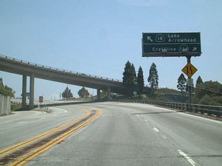 Northbound California 18 meets California 138 near Crestline at a trumpet interchange. This unique interchange barely fits into this location on top of the mountain grade. This interchange marks the eastern terminus of California 138. From here, northbound California 18 changes directions to eastbound California 18 en route to Lake Arrowhead and Big Bear City. At Big Bear City, California 18 changes directions a second time, and starts to head north once again. Upon reaching Lucerne Valley, the highway changes directions once last time at its "bump" with California 247. California 18 heads west through Apple Valley and Victorville before terminating at its junction with ... California 138, the same road that is shown at this interchange near Crestline! Together with California 138, California 18 north/east of Crestline forms a loop tour through mountain and desert country.