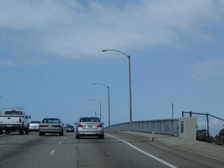 Three lanes carry Second Street over a channel into Long Beach; turquoise colored bridge railings line the highway. The next interchange with with Appian Way.
