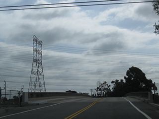 The old alignment of California 22 over the San Gabriel River is College Park Drive. The original bridge complete with old concrete railing can be found via the Studebaker Road off-ramp from California 22 west. This bridge now serves as the primary route into a small suburban residential community (Edison Park) bounded by Interstate 405, California 22, and the San Gabriel River. These views look east on College Park Drive.