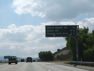 After traffic from California 118 (Simi Valley Freeway) merges with the California 23 on-ramp from Los Angeles Avenue, the Moorpark Freeway begins to head south toward Thousand Oaks. An interchange sequence sign provides the distance to the first three exits on California 23 (Moorpark Freeway) south: Exit 19, Tierra Rejada Road; Exit 17, Olsen Road; and Exit 16, Sunset Hills Boulevard.
