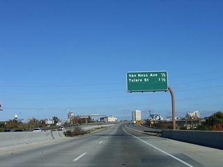 The downtown skyscrapers of Fresno come into view ahead as we continue on an elevated viaduct. This mileage sign provides the distance to the next two exits along California 41 (Yosemite Freeway) north: Exit 126B, Van Ness Avenue and Ventura Street (old alignment of California 180) to downtown Fresno and Exit 127, Tulare Street and Divisadero Street.