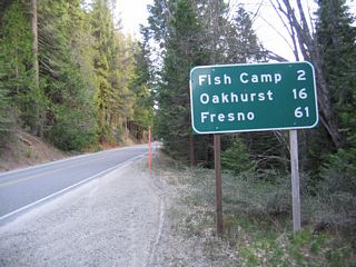 A mileage sign near a turnout provides the distance to Fish Camp (two miles), Oakhurst (16 miles), and Fresno (61 miles).