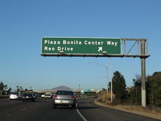 Eastbound California 54 reaches Exit 3, Plaza Bonita Center Way/Reo Drive. Plaza Bonita Center Way leads south to connect with Sweetwater Road, while Reo Drive leads north into Paradise Hills, a community of San Diego.