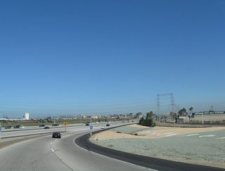 Rock artwork offers urban relief in the interchange pocket between the transition ramp from California 54 west to Interstate 5 north (via Exit 1B). Below, multiple lanes of Interstate 5 hustle by as traffic California 54 west prepares to merge into this major freeway.