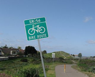 For much of the route between Carmel Valley Road (Exit 3) and Interstate 15, a bike path closely follows California 56. Entrances to the bike path are located at major intersecting roads, including this entrance at Salmon River Road looking west. A survey marker designates the freeway as the property of the state highway department and lists construction as occurring in 1992 (at least at this location).