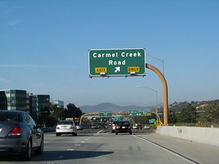 Upon turning east, California 56 splits into a collector distributor lane arrangement. The right lane joins the c/d lane, while the left two lanes continue east on California 56. Traffic merges onto California 56 from El Camino Real. The next exit (Exit 1) serves Carmel Creek Road, which connects to the community of Carmel Valley.