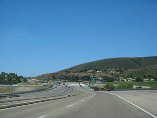 Crossing over Rancho Carmel Drive and Sabre Springs Parkway, the Interstate 15 and Ted Williams Parkway interchange comes into view. The westbound side reduces to two through lanes. Merge into the right lane for the connection to Interstate 15 (Escondido Freeway) north (Exit 9B).
