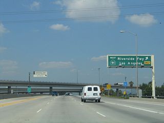 As part of the stack interchange, northbound California 57 reaches Exit 5B, the ramp to westbound California 91 (Riverside Freeway). Note that the control city is Los Angeles, which can be considered true in the sense that California 91 enters Los Angeles when it crosses Interstate 110. In addition, California 91 enters Los Angeles County after departing La Palma and entering Cerritos west of Interstate 5. In the vicinity of the county line, the California 91 freeway name changes to the Artesia Freeway.