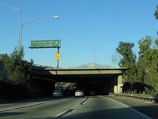As California 60 passes overhead, northbound California 57 enters a brief tunnel to pass under the Pomona Freeway.