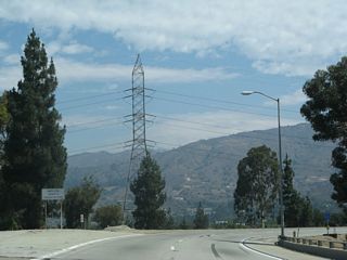 This view shows the ramp from California 57 north to California 210 east. A tall Los Angeles Department of Water and Power transmission line tower is visible as the ramp curves east.