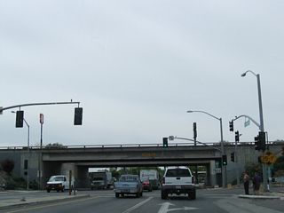Southbound California 59 (V Street) travels two blocks between California 99 Business and the California 99 freeway in Merced. Approaching the elevated freeway, the first traffic signal links to 14th Street, which only travels one-way northwestbound. Look for a right turn onto California 99 north. After passing under the freeway, California 59 will connect to California 140 west to Gustine. Bear right on California 59 (V Street) to join California 140 west. Turn left after passing under the freeway for California 59 south, California 99 south, and California 140 east. California 59 will follow 13th Street south along the frontage road.