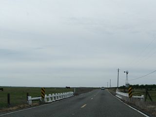 An older bridge, complete with white, wooden railing, is located on CR J-59 just north of Snelling. Some agricultural and ranching operations are visible from the county road.