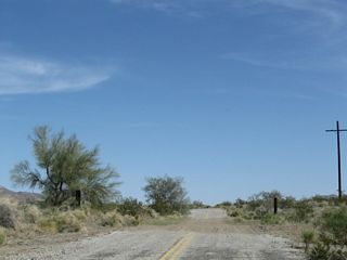 Floodwaters have ravaged segments of old Box Canyon Road, leaving only gravel and sand left on top of the original roadbed. The newer alignment of old U.S. 60-70 along Pinto Road overtakes Box Canyon Road just ahead.