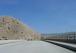 A narrow concrete bridge carries Whitewater Cutoff Road over Interstate 10 at Exit 114. An old bridge crosses the Whitewater River around the bend ahead.