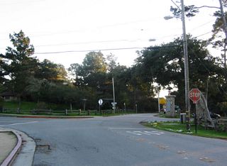 Southbound Asilomar Avenue at the entrance to the Asilomar Conference Grounds in the city of Pacific Grove just south of the Point Pinos Lighthouse. California 68 begins its eastbound journey at this four-way stop intersection. A left turn connects to eastbound Lighthouse Avenue; a right turn enters the conference grounds.