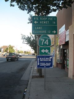 Traveling south on D Street in the city of Perris prior to the California 74 (Fourth Street) intersection was this mileage sign. It was removed by 2009 during a redevelopment project to improve the streetscape in downtown Perris. Note that Interstate 215 was referred to as &quot;Temporary Interstate 15E.&quot; This referred to a designation that has not been used for the Interstate 215 corridor since 1982, when Interstate 15E (and Temporary Interstate 15E) were decommissioned in favor of Interstate 215.