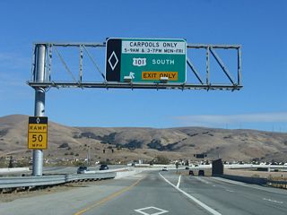 The carpool lanes and main lanes split at this point, with the right two lanes are for through traffic and the left lane is for high occupancy vehicles (during regulated hours). On the hill in the distance are Pacific Gas and Electric 500kV power lines that connect Path 15 in the Central Valley with the Moss Landing Power Generating Station on the coast northwest of Salinas.