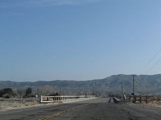 Beyond the intersection with Irwin Road, N 1st Avenue (Historic U.S. 91) crosses another historic bridge over a tributary to the Mojave River. This span features white wooden railing and  concrete divoted curbing.