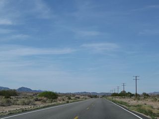 As the mountains pull away to the northwest, U.S. 95 straightens out and continues alongside the river. A mirage brings the appearance of a reflection (of the distant car) into non-existent water on the pavement.