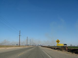 Continuing east, California 98 approaches Vencill Road. The smoke in the background is the result of farmers burning their fields to increase productivity. The fires are most common during the winter months, and in some cases, they can cause poor visibility on the highway.