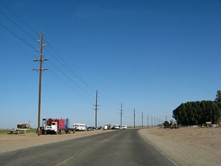 More agricultural fields line California 98 as the two-lane highway continues east. The white school buses are used to transport day laborers to the fields to harvest the fruit and vegetables grown in the valley.