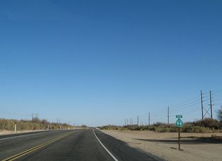 A California 98 east reassurance shield is posted as the highway continues into the desert. The All-American Canal continues alongside the highway to the south, and the power lines follow it to the next hydroelectric generating station. (Power is generated as the water cascades from the elevation of the Colorado River west to the Imperial Valley which lies below sea level.)