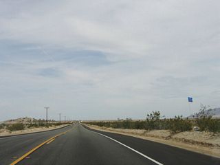 These blue flags, which are posted next to containers every several hundred feet, offer water to travelers (legal or illegal) who pass through the Yuha Desert. The word "water" is written in English, Spanish, or both languages.