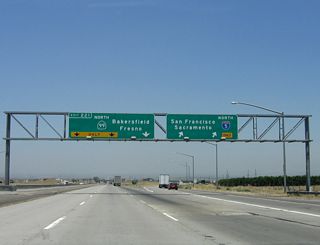 Interstate 5 and California 99 split at Wheeler Ridge, and the two freeways diverge: Interstate 5 heads northwest, while California 99 continues north toward Bakersfield. Stay left for Exit 221, which connects from Interstate 5 north to the main lanes of California 99 north. The right two lanes continue as Interstate 5 by sweeping to the right and then flying over California 99.
