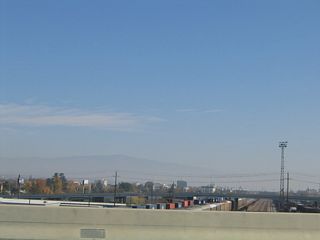 This view looks east from California 99 toward downtown Bakersfield as well as the railroad yard. After passing over the railroad tracks, California 99 will pass over Truxtun Avenue (no access) and then will pass over the Kern River, which flows out of the Sierra Nevada (Kern River Canyon) west into the southern Central Valley.