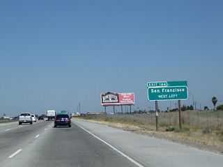 The next exit along northbound California 99 is Exit 166, California 152 west to Los Banos, Gilroy, Santa Cruz, San Jose, and San Francisco (left exit). This upcoming interchange will mark the eastern terminus of California 152. This sign used to be located further north but was relocated here after the Avenue 22 1/2 intersection was removed from service.