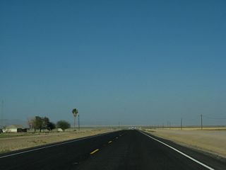 California 115 proceeds east past farmlands, then passes by an H-frame power tower. Soon thereafter, 115 will make a sharp turn south.