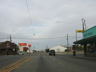 At this intersection in downtown Holtville, California 115 and Imperial County Route S-32 split. Imperial County Route S-32 turns north onto Holt Road. California 115 continues east along Old U.S. 80/Evan Hewes Highway. Turn north on CR S-32 to Holt Park. Within the park are a few interesting highway artifacts, including a replica Auto Club of Sourhern California mileage sign along with some comemmorative plaques.