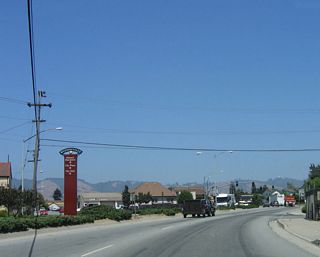 A city of Watsonville wayfinder sign is posted in the median after the Walker Street traffic signal. To downtown, city hall, and city plaza, continue straight ahead on eastbound California 129.